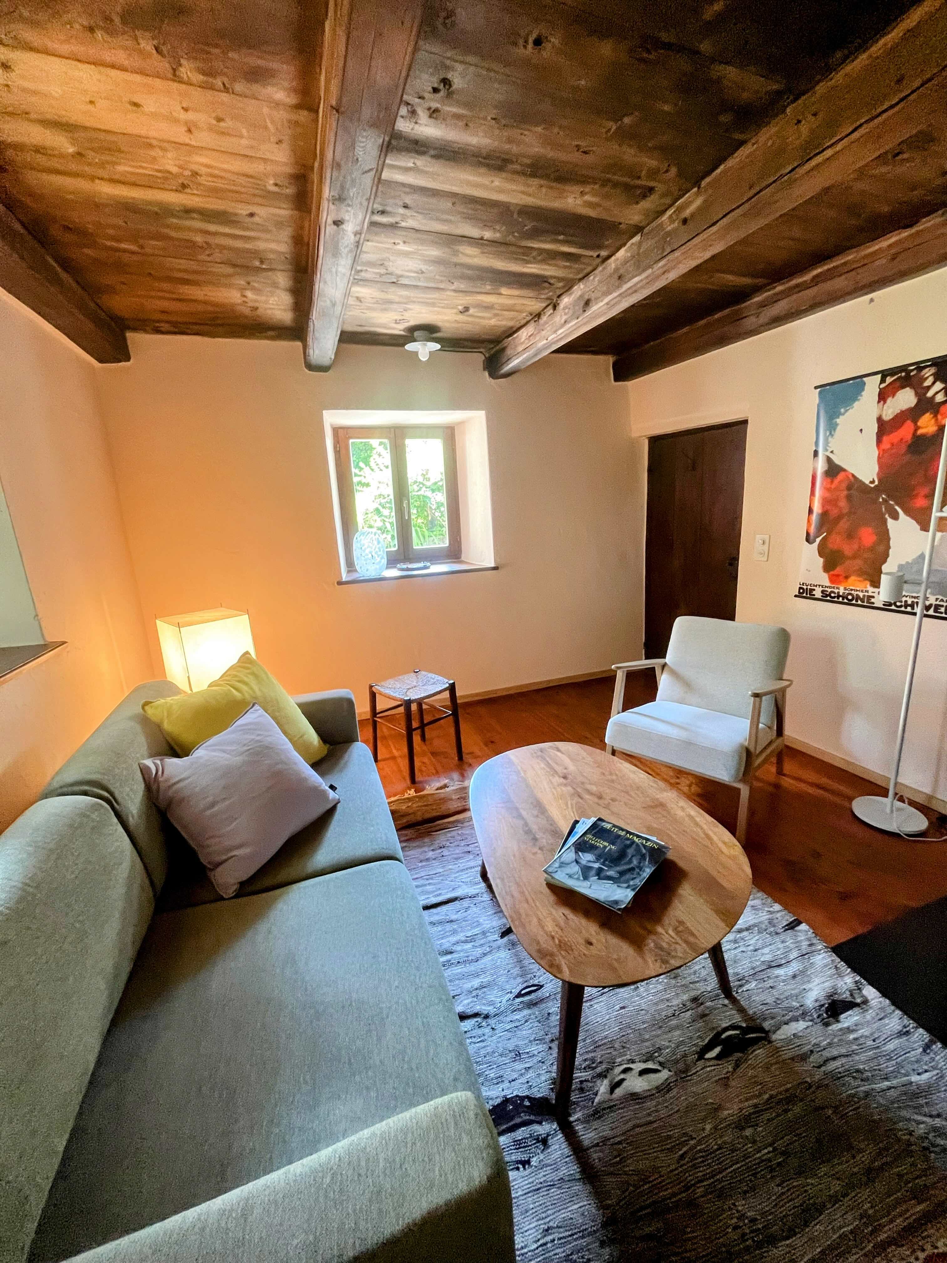 Wohnzimmer mit Sofa, Holzbalken und warmer Beleuchtung